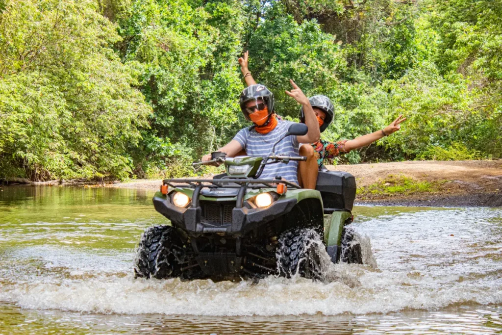 Two travelers crossing a tropical river on ATVs during an Outback Quads tour in La Fortuna Costa Rica.