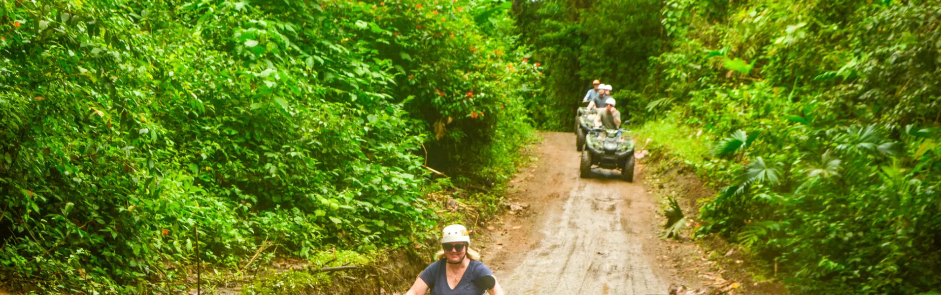 Group riding ATVs along a jungle trail surrounded by lush rainforest during a guided tour in La Fortuna, Costa Rica.