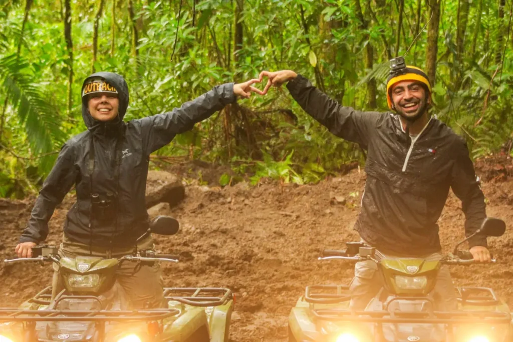 Two friends celebrating while riding ATVs through muddy jungle trails during an adventure tour in La Fortuna, Costa Rica.