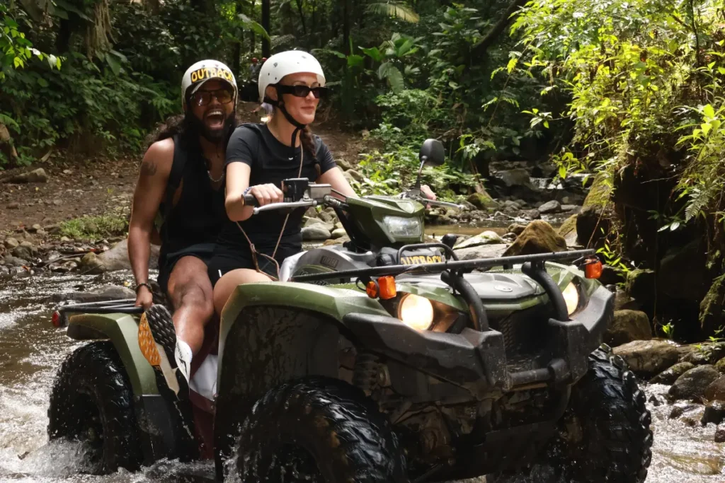 Couple riding an ATV through a shallow river during a guided jungle tour in La Fortuna, Costa Rica.