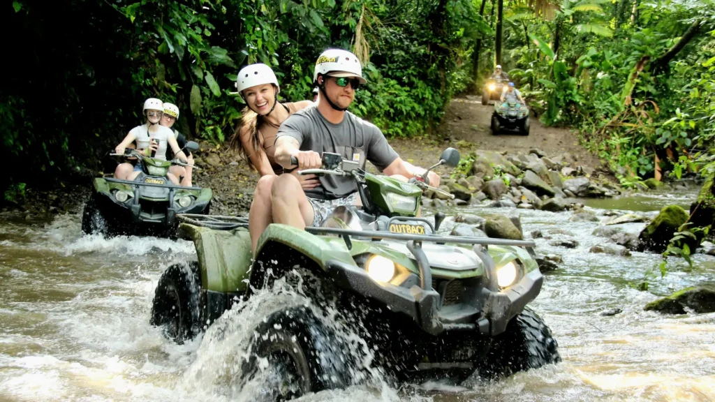 Couple riding an ATV through a shallow river during a rainforest tour in La Fortuna, Costa Rica.