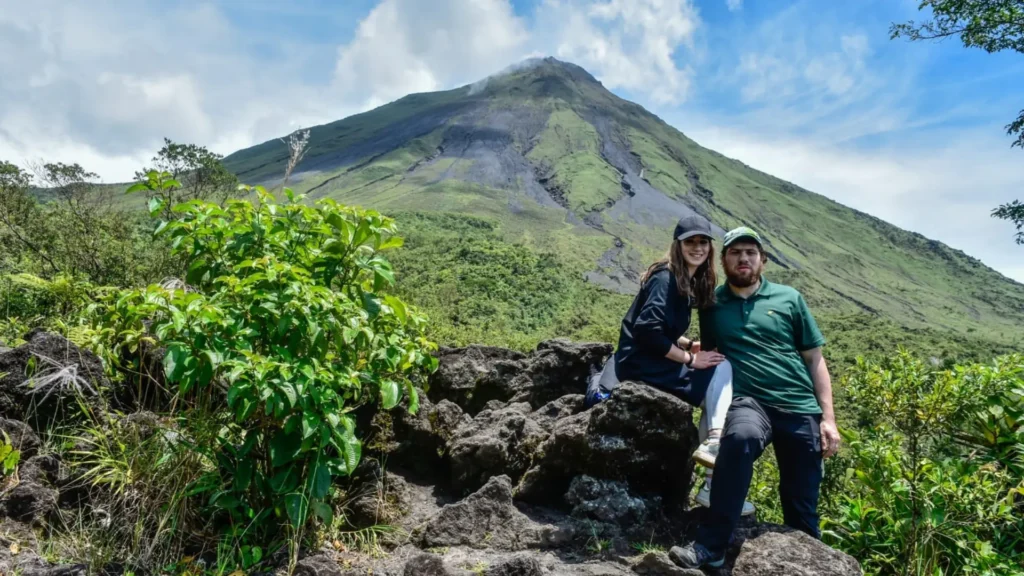 Travelers standing on volcanic rocks with Arenal Volcano in the background near La Fortuna, Costa Rica.