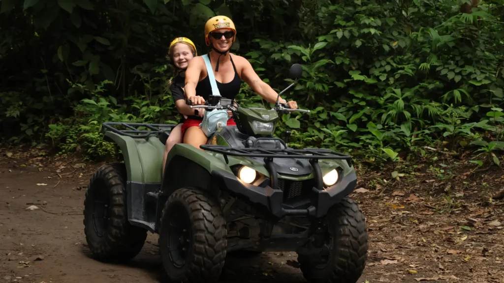 Girl riding as a passenger on an ATV through rainforest trails near Lake Arenal during the LakeSide & River Crossing ATV Tour